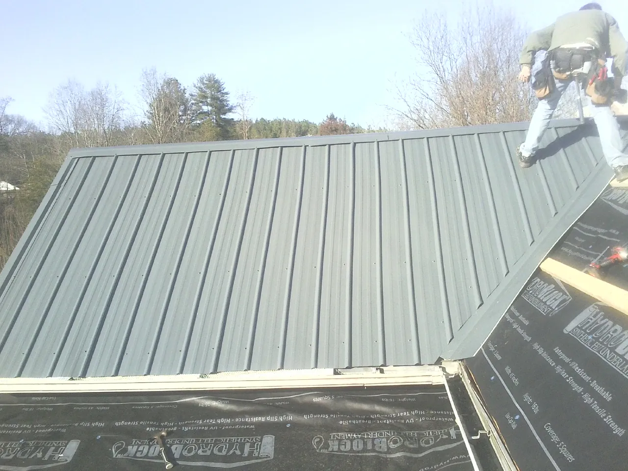 Crew installing dark green standing seam panels over synthetic underlayment in Napoleon