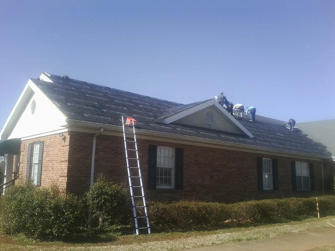 Crew tearing shingles off a brick ranch roof with a ladder set — Emergency Roof Repair work by our crew in Napoleon