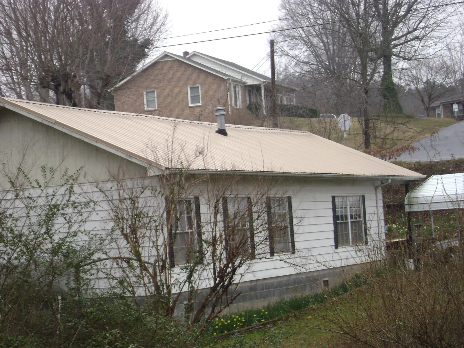 Tan metal roof on a white sided house set into a hillside — Commercial Roofing by Roofing Brothers in Napoleon