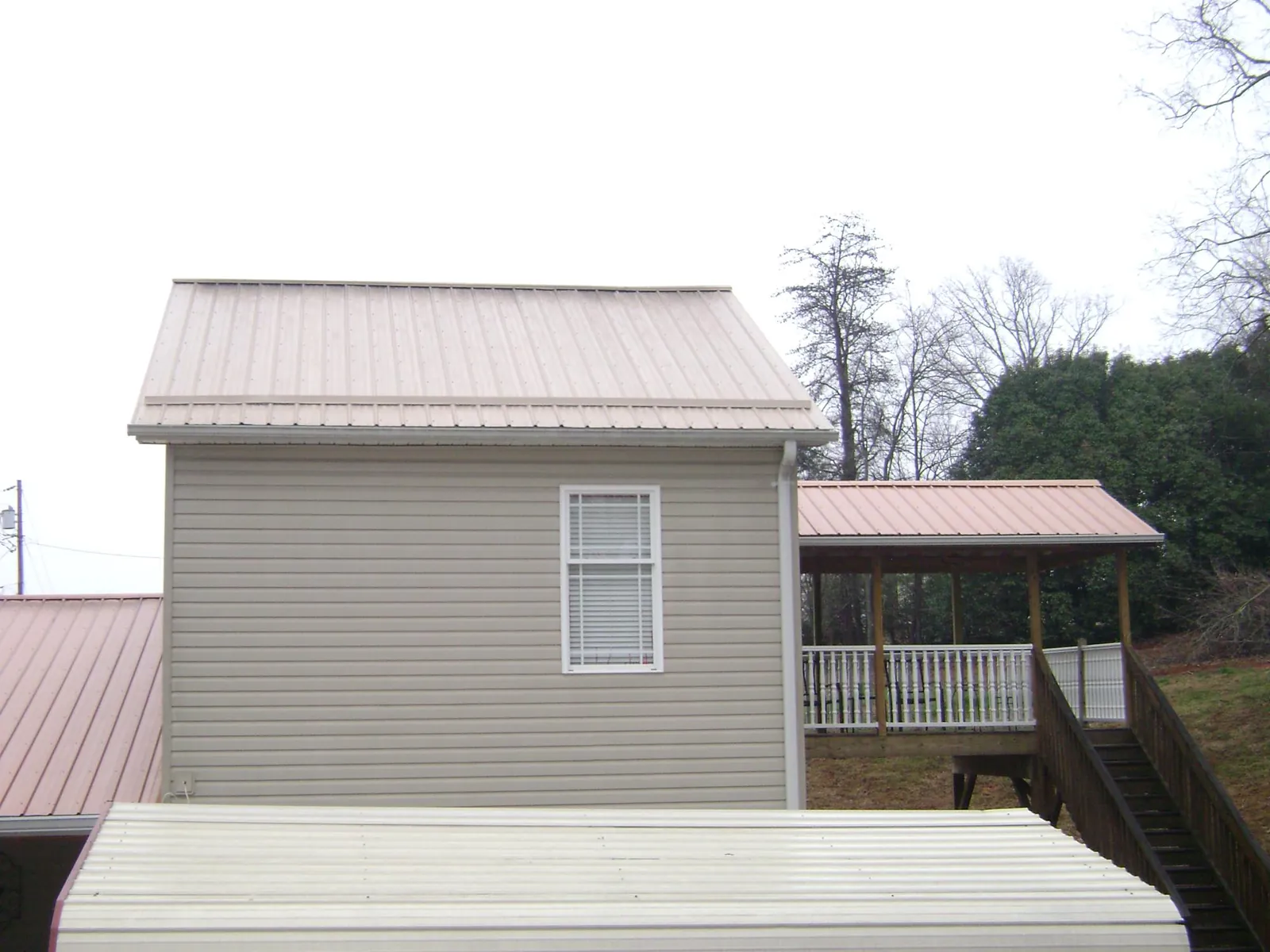 Tan metal roofs on a two story addition and attached porch, from a Roof Replacement job in Napoleon